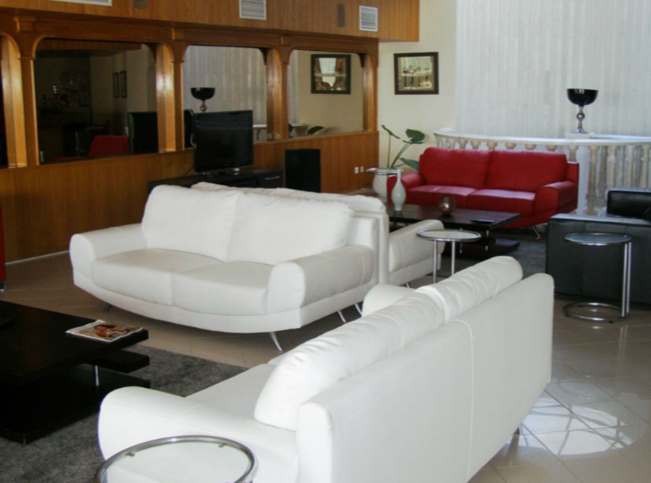 Een moderne woonkamer met een witte bank, een rode bank en een zwarte fauteuil. Er is een salontafel, een klein bijzettafeltje en een televisie.