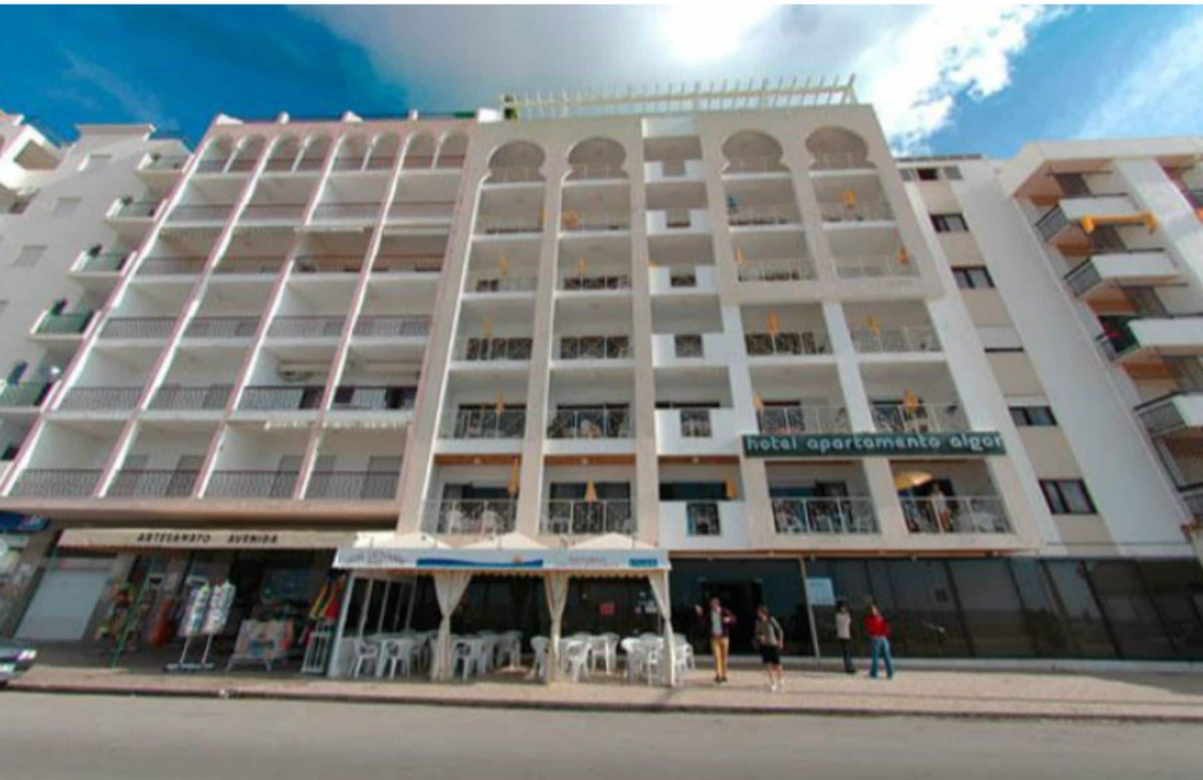 A multi-story hotel with balconies, a ground-level restaurant, and outdoor seating.