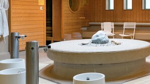 Un sauna avec un banc circulaire en pierre, des chaises blanches et un mur en bois doté de fenêtres.