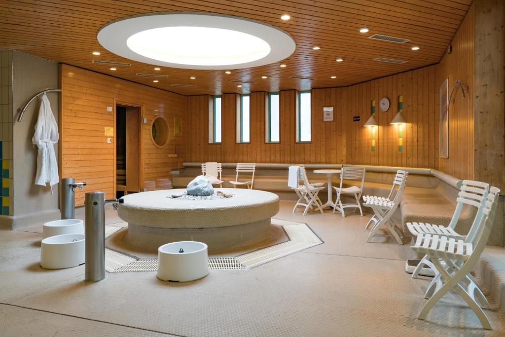 A sauna room with a circular hot tub, white chairs, and a wooden ceiling.