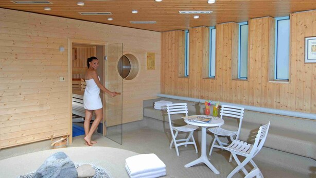 Une salle de spa moderne avec des murs en bois, un sauna, une table de massage et un petit coin salon avec une table et des chaises.