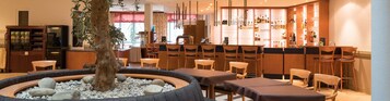 A restaurant with a central fire feature, multiple seating areas, and a bar with a variety of bottles and glasses.