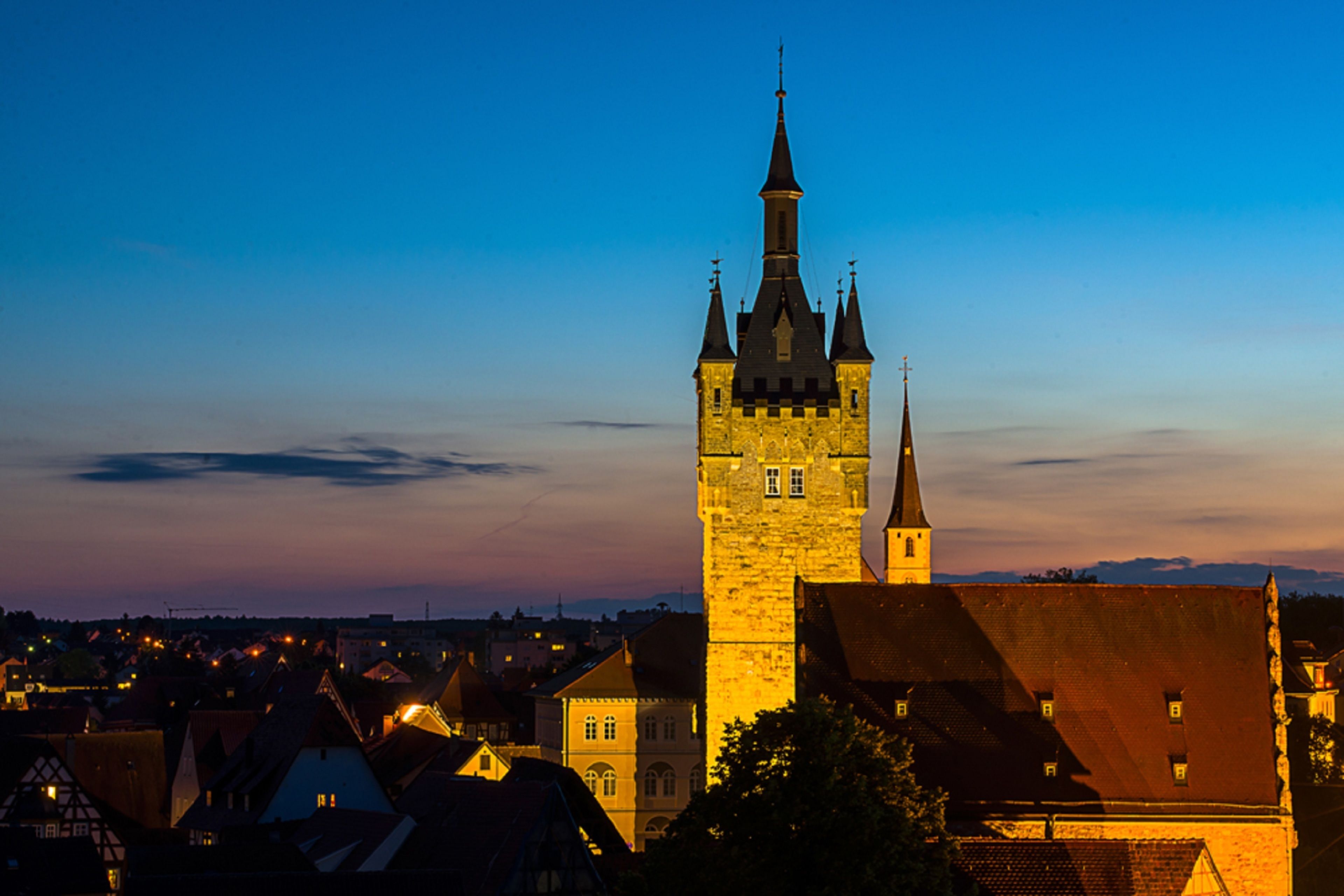 A historic tower with a spire, surrounded by traditional buildings with sloped roofs.