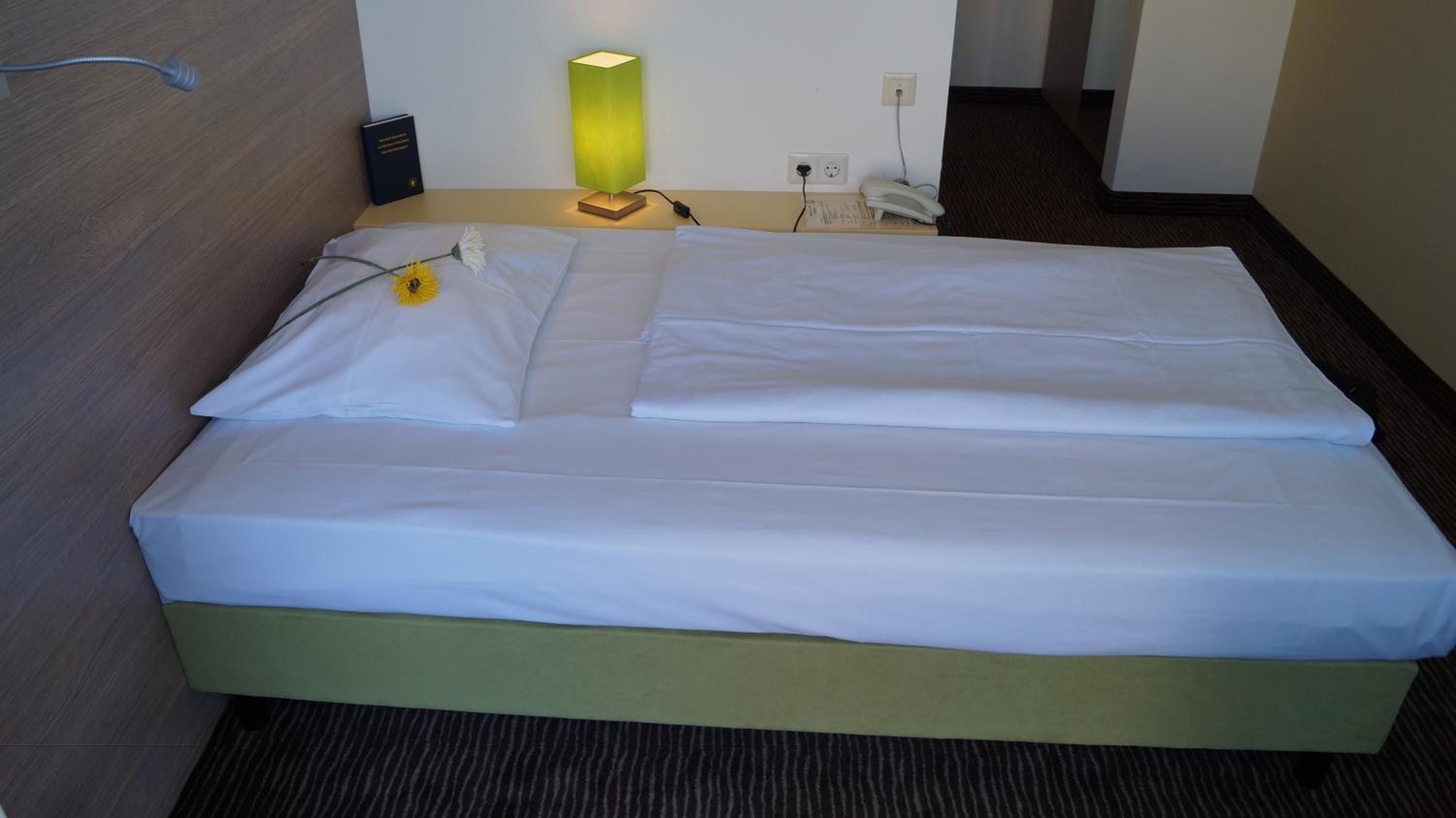 A hotel room with a bed, a bedside lamp, a telephone, and a power outlet.