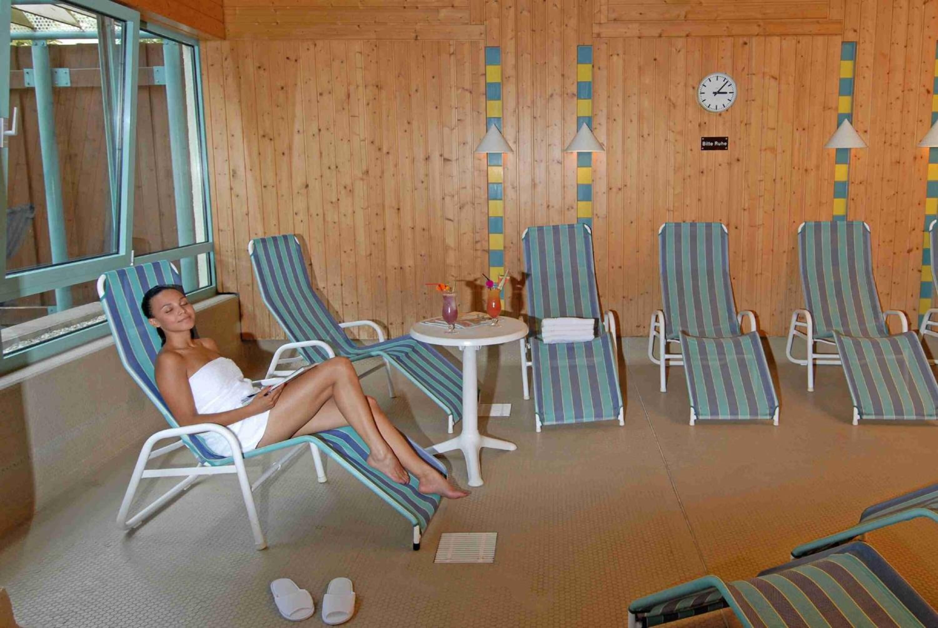 A room with wooden panel walls, striped lounge chairs, a small table with a drink, and a clock on the wall.