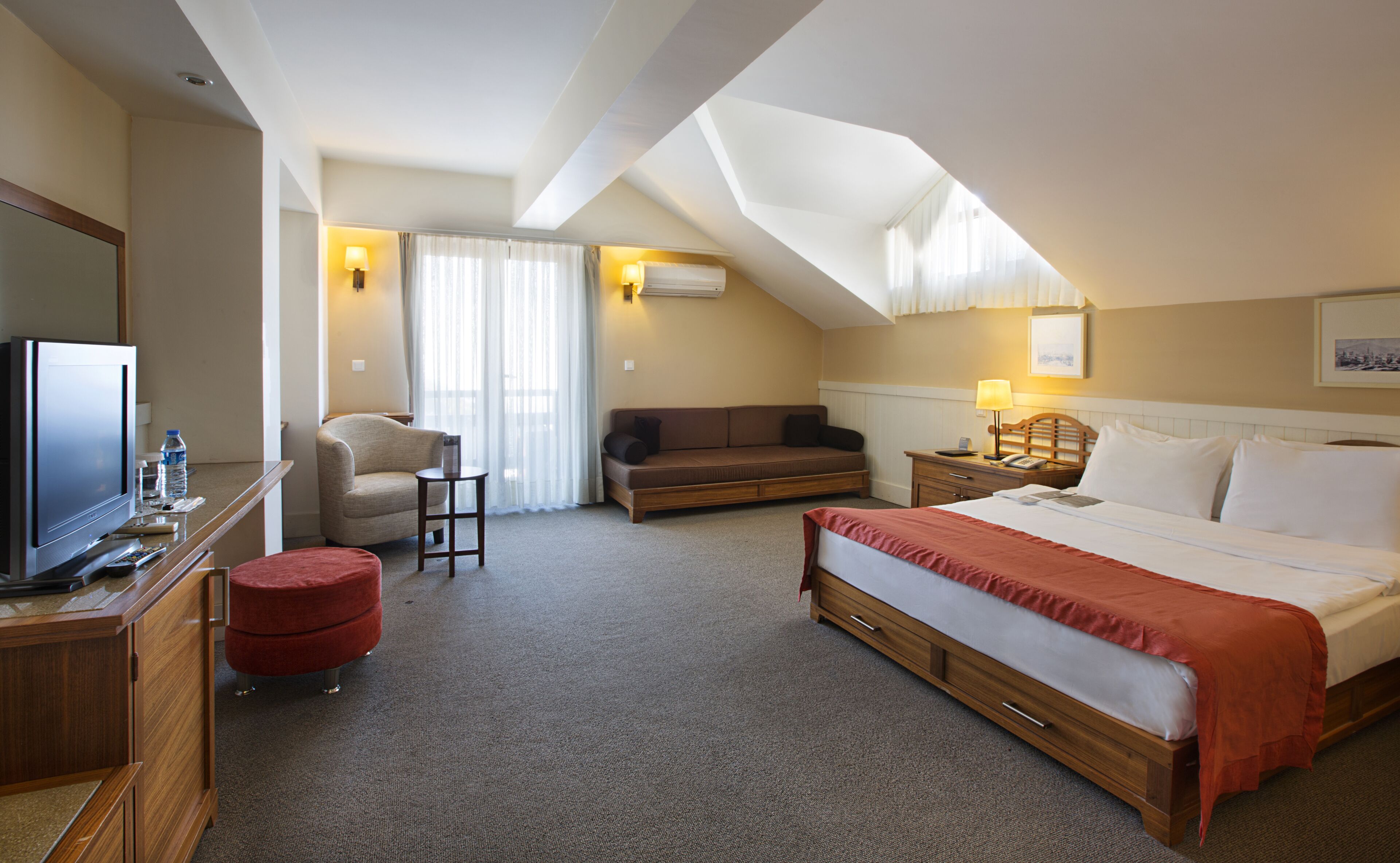 A hotel room with a bed, a sofa, a TV, a desk, and a chair.