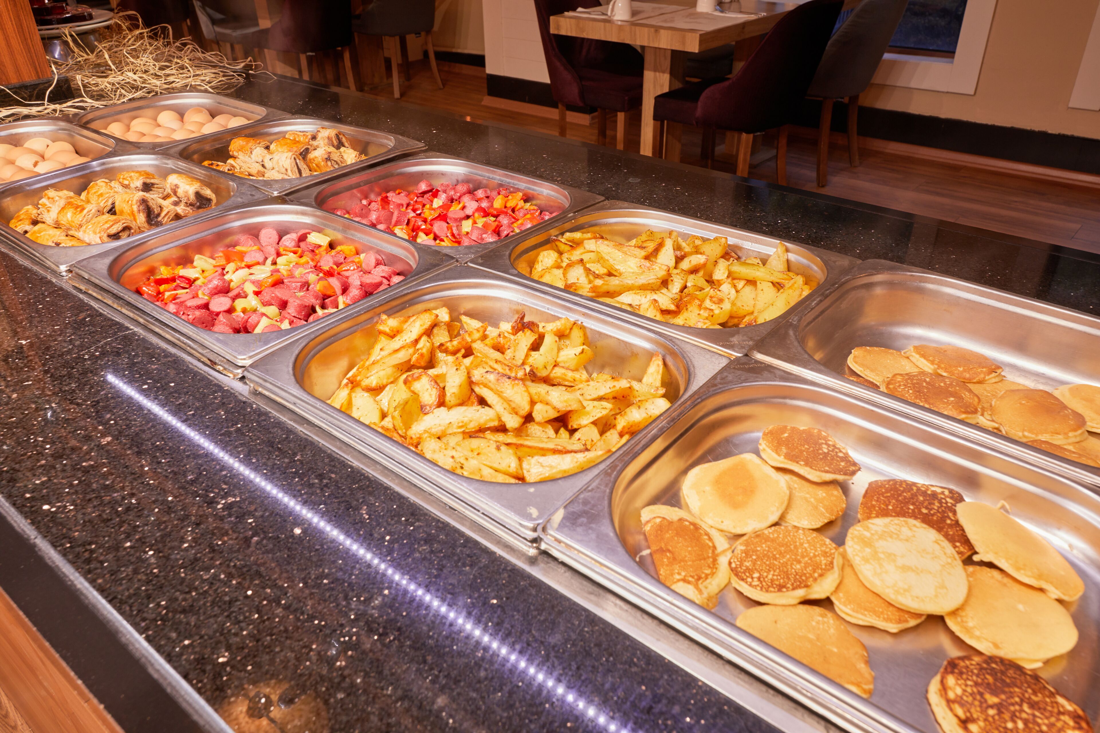 A buffet with various food options including meats, potatoes, and pancakes.