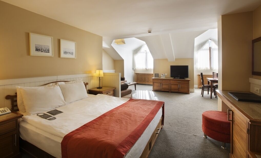A hotel room with a large bed, a desk, a TV, and a dining area.