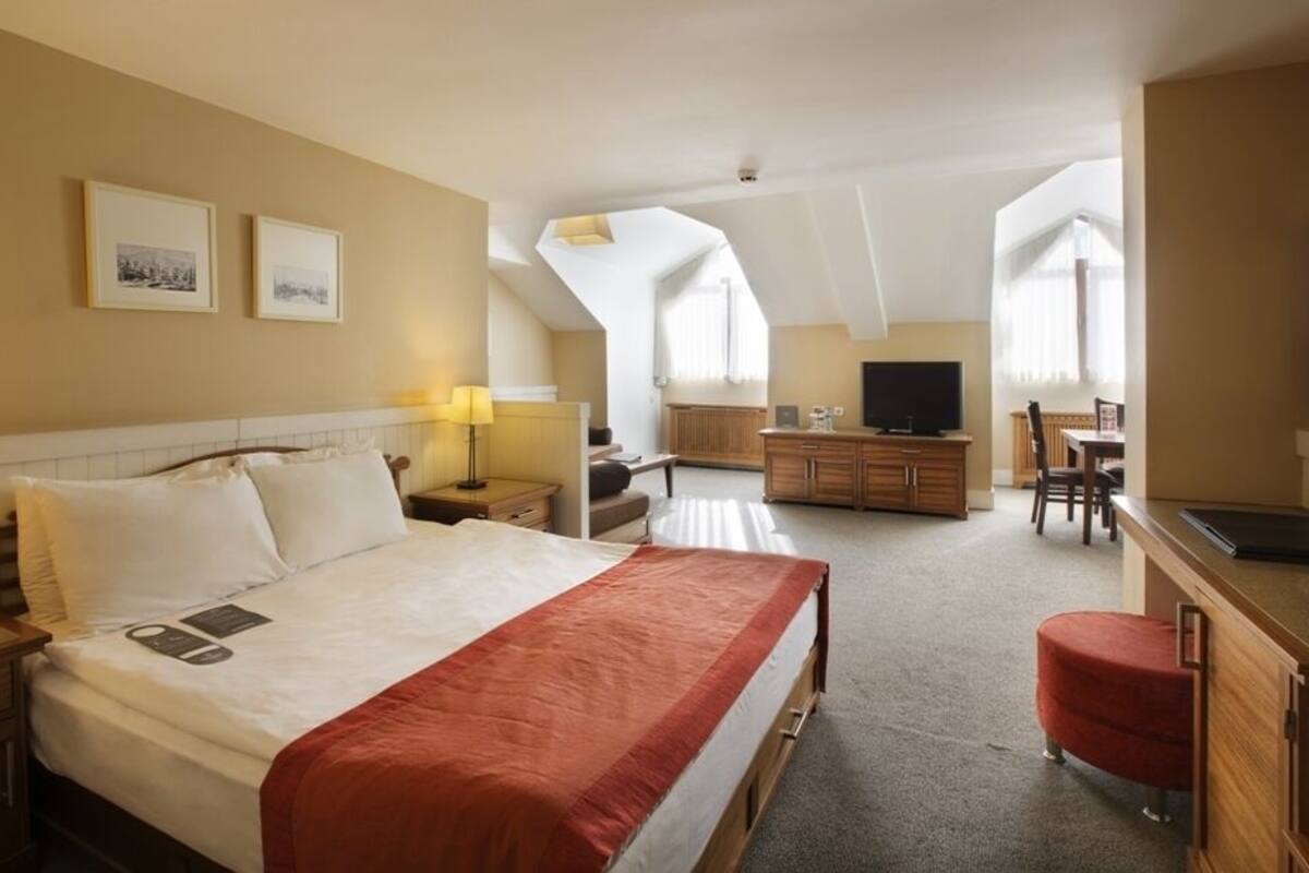 A hotel room with a large bed, a desk, a TV, and a dining area.