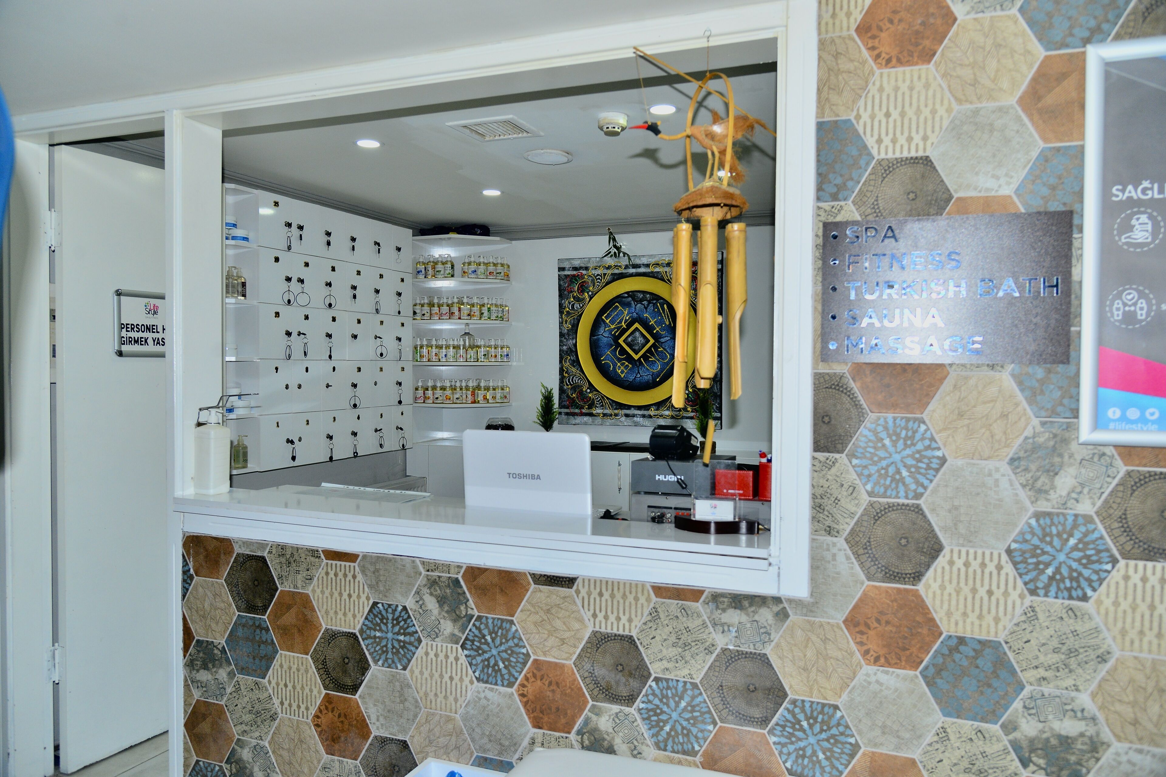 A reception area with a counter, a sign listing amenities like spa and massage, and a wall with hexagonal tiles.