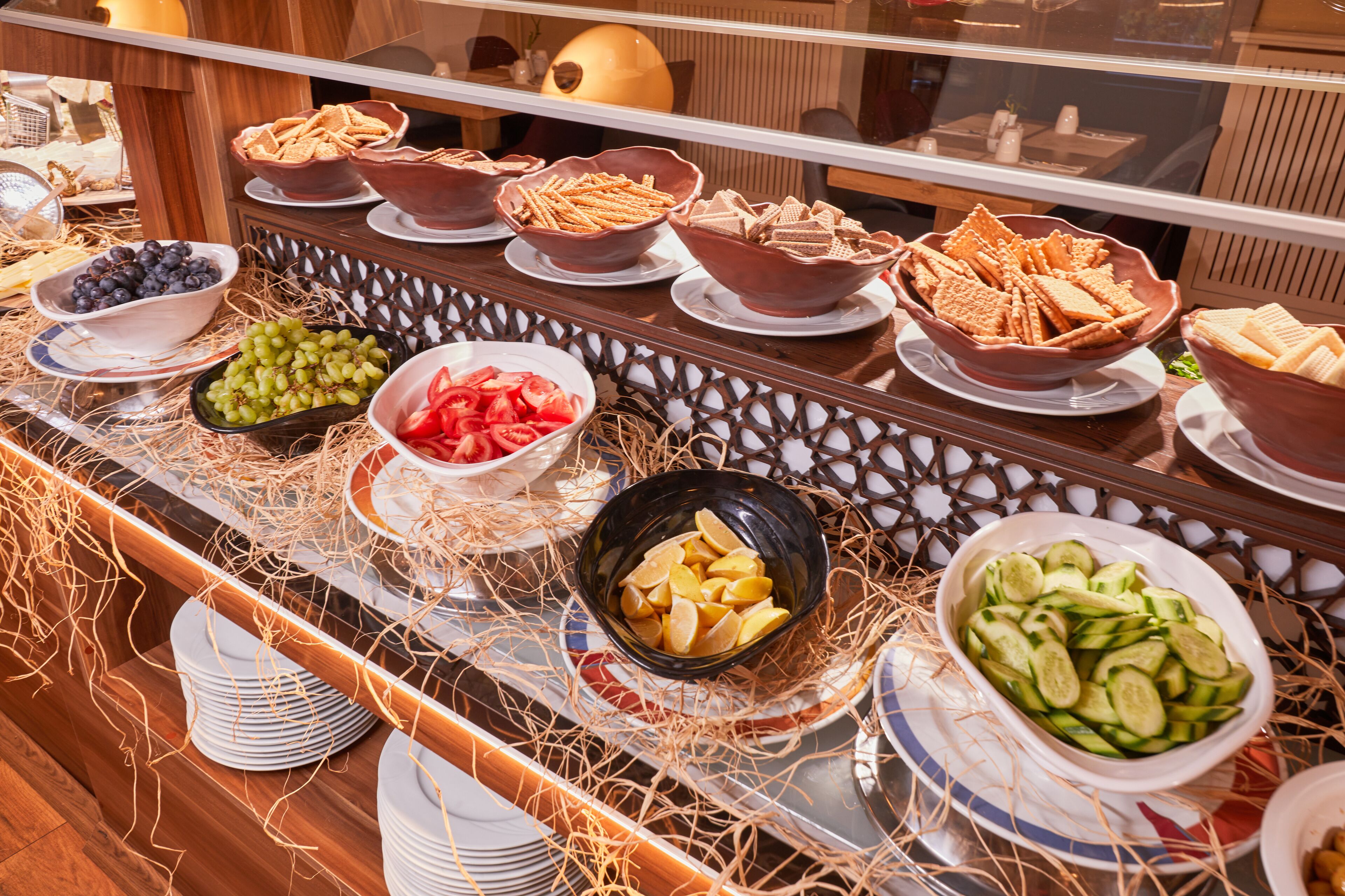 A buffet with various food items including grapes, tomatoes, cucumbers, and crackers.