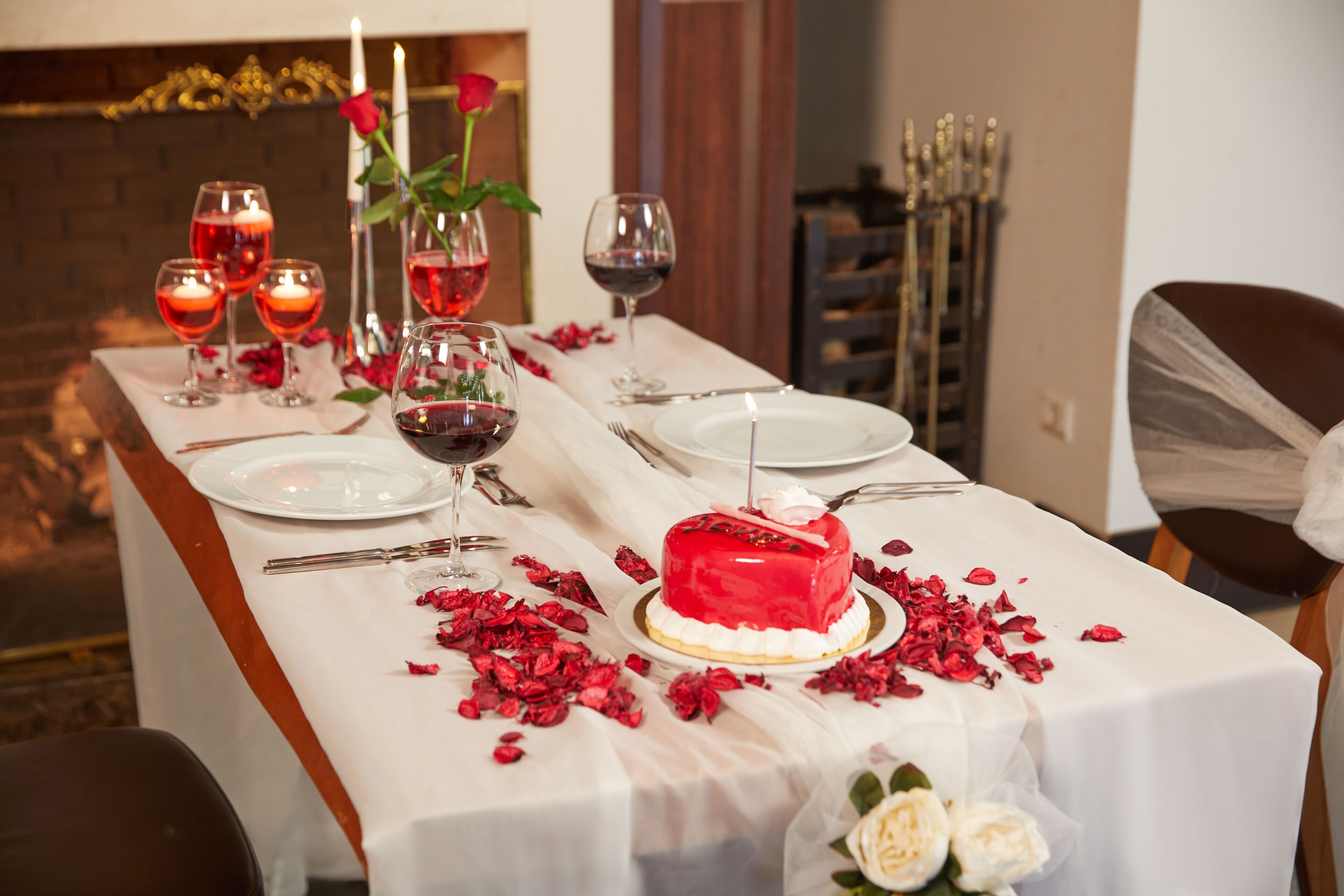 Una mesa lista para una cena romántica, con un pastel rojo, copas de vino y rosas.