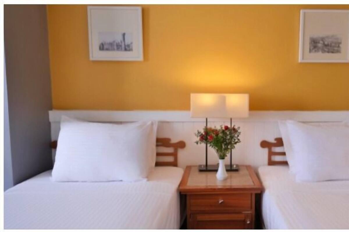 A double bed with white linens, a bedside table with a lamp, and a vase with flowers.