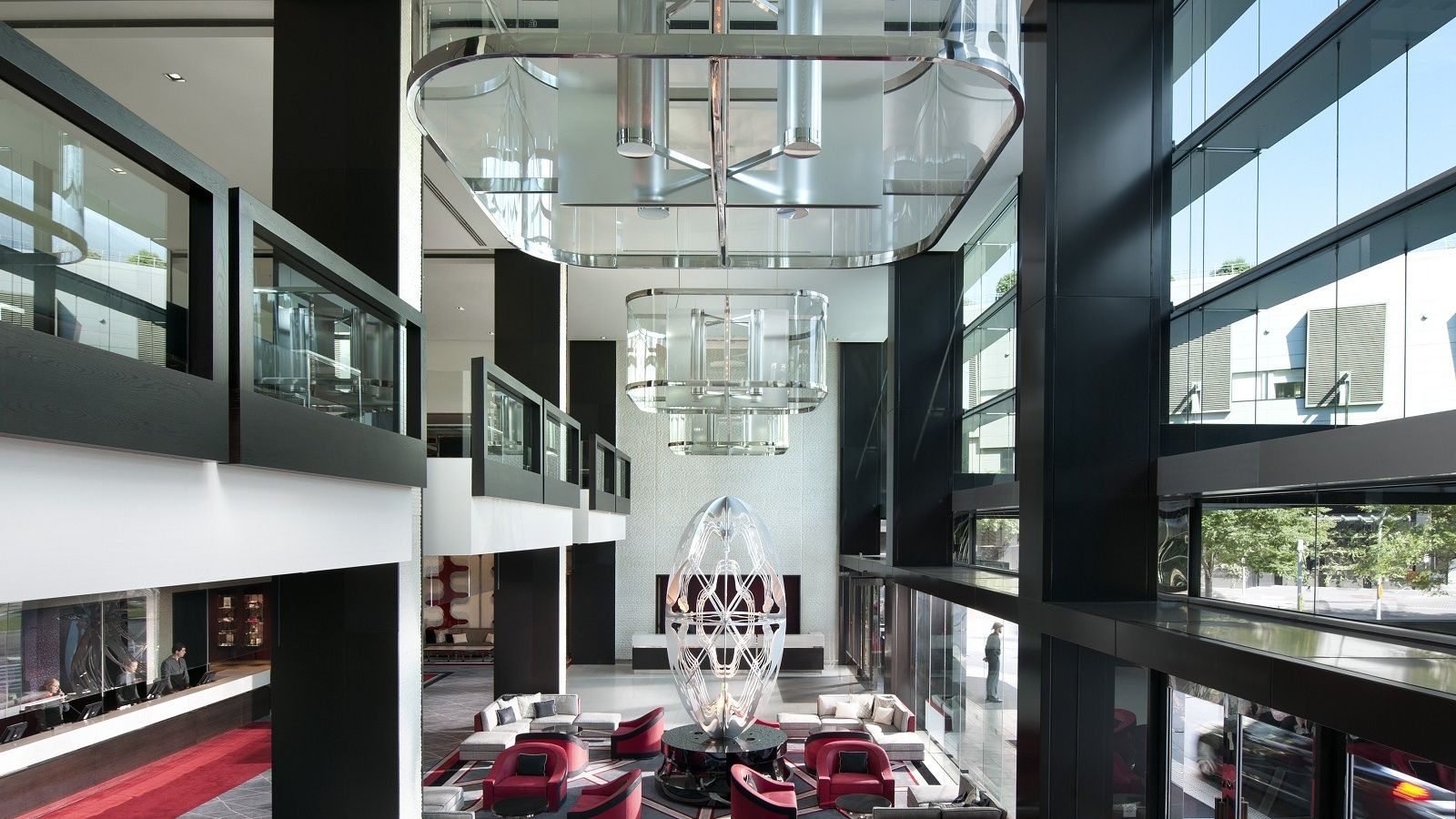 A modern interior with a central glass sculpture, multiple levels with glass railings, and a red carpeted area.