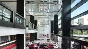 Un intérieur moderne avec une sculpture en verre au centre, plusieurs niveaux dotés de rampes en verre et un espace recouvert d’un tapis rouge.