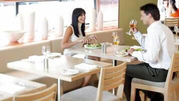 Un restaurante con sillas y mesas de madera, un ventanal con vistas y una persona sosteniendo un vaso.