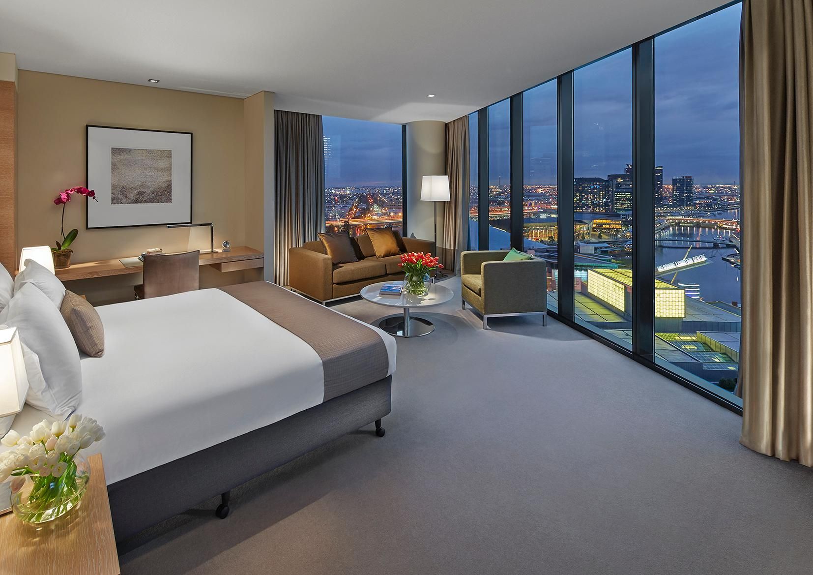 Habitación de hotel moderna con una cama grande, un sofá, una mesa de centro y vistas a un paisaje urbano.