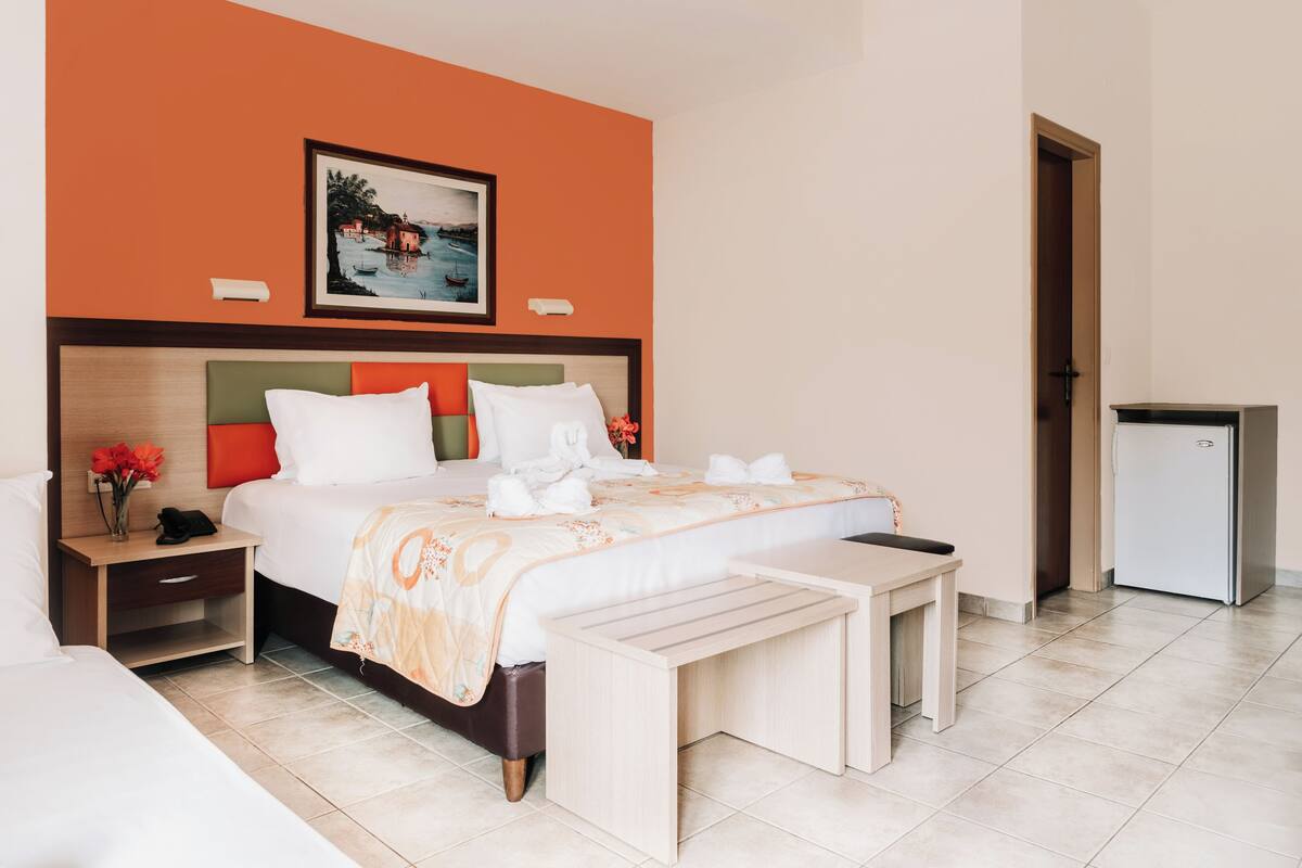 A hotel room with a bed, bedside tables, a small refrigerator, and a painting on the wall.