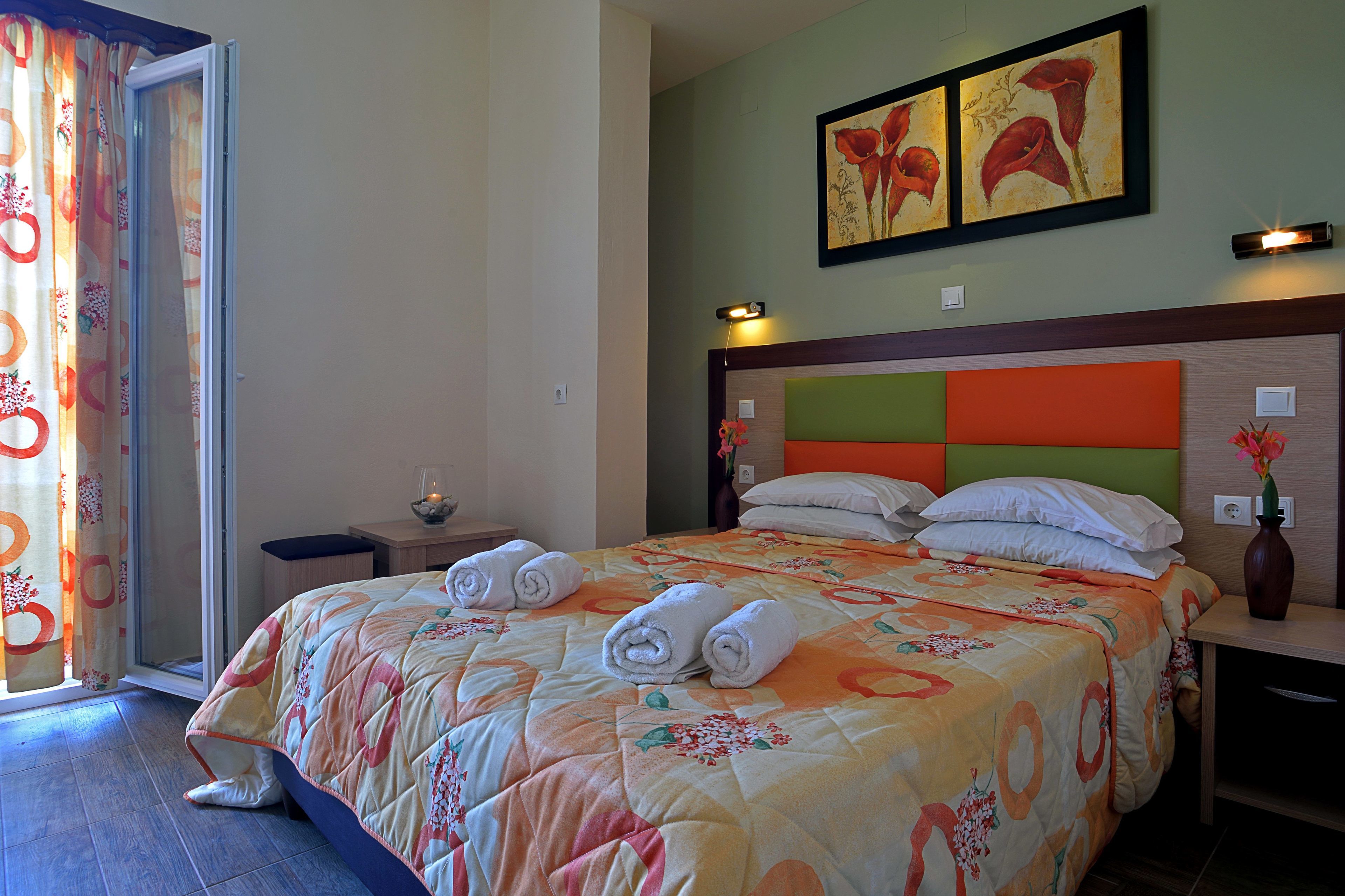 A hotel room with a bed, a nightstand, a vase with flowers, and a painting on the wall.