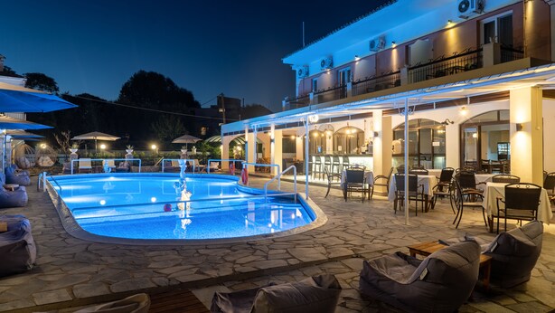 A pool area with lounge chairs and tables, a covered patio with outdoor seating, and a building with multiple windows and balconies. - Maltezos (Corfu)