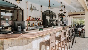 A bar area with a stone counter, multiple hanging light fixtures, and a variety of bottles and glasses on shelves. - Maltezos (Corfu)