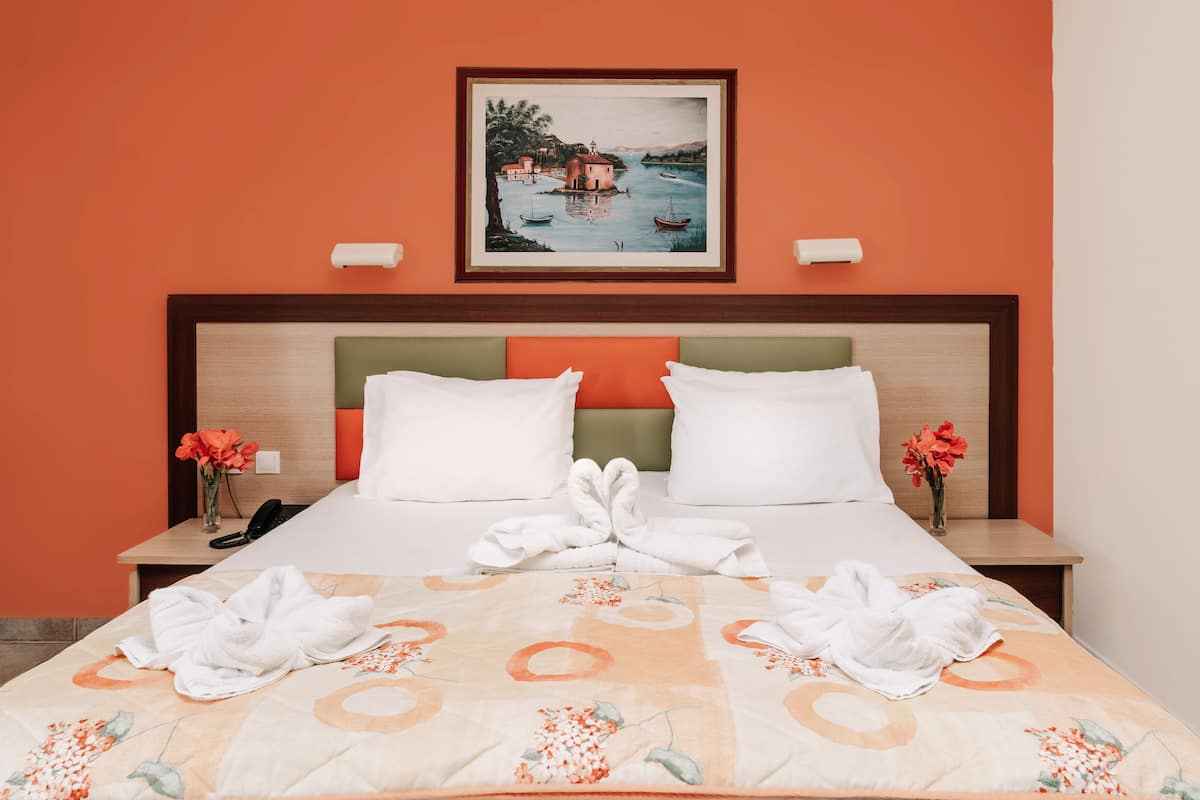 A hotel room with a bed, two pillows, a painting above the bed, and a vase with flowers on the nightstand.