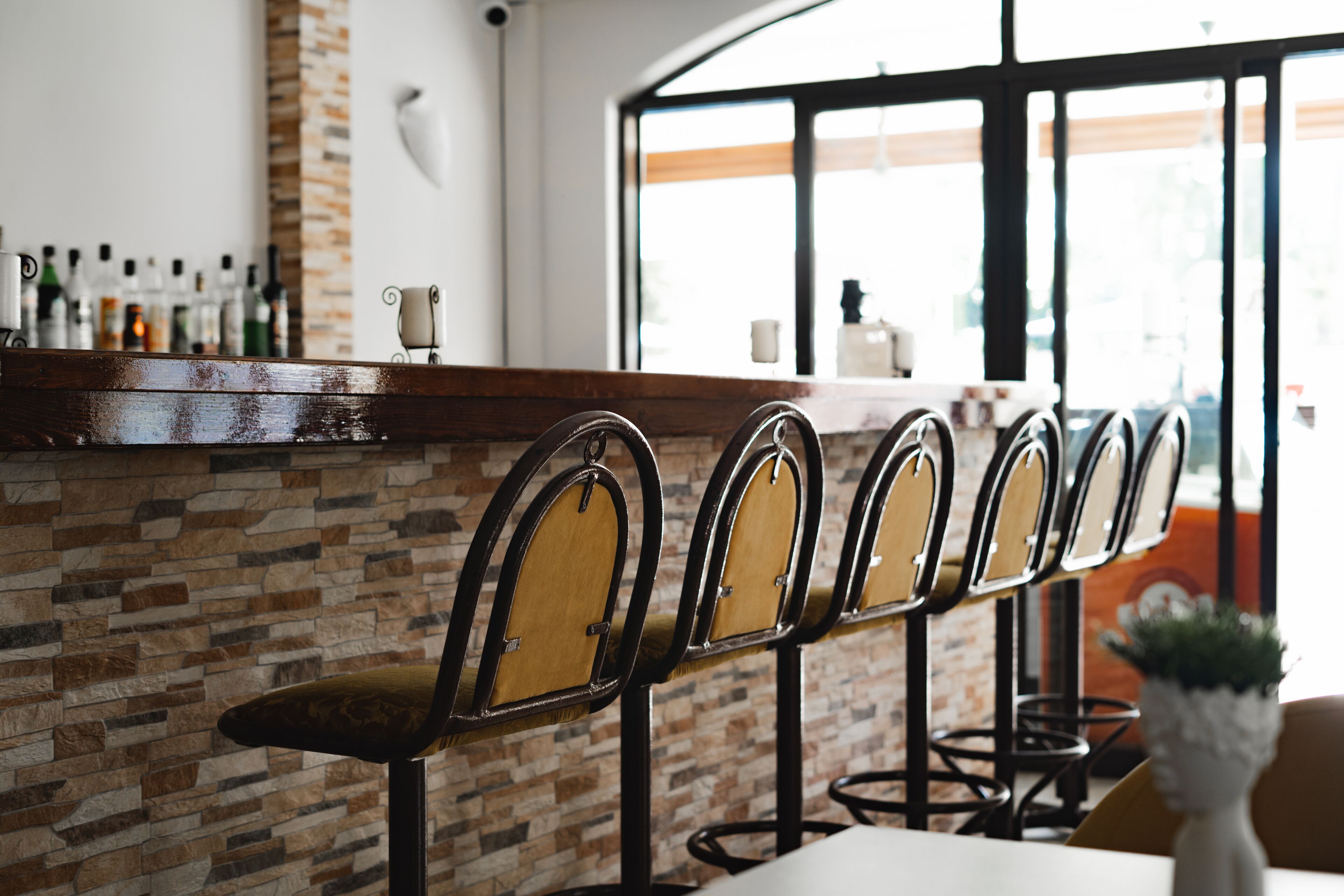 A bar area with a brick wall, wooden chairs, and a white countertop with various bottles.