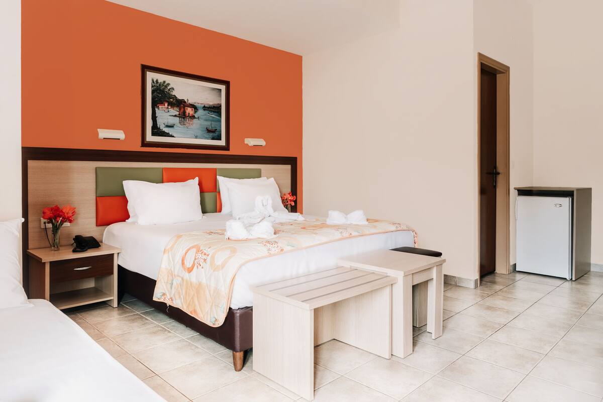 A hotel room with a bed, bedside tables, a small refrigerator, and a painting on the wall.