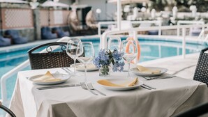 A table set for dining with a pool view, including plates, cutlery, and a vase of flowers. - Maltezos (Corfu)