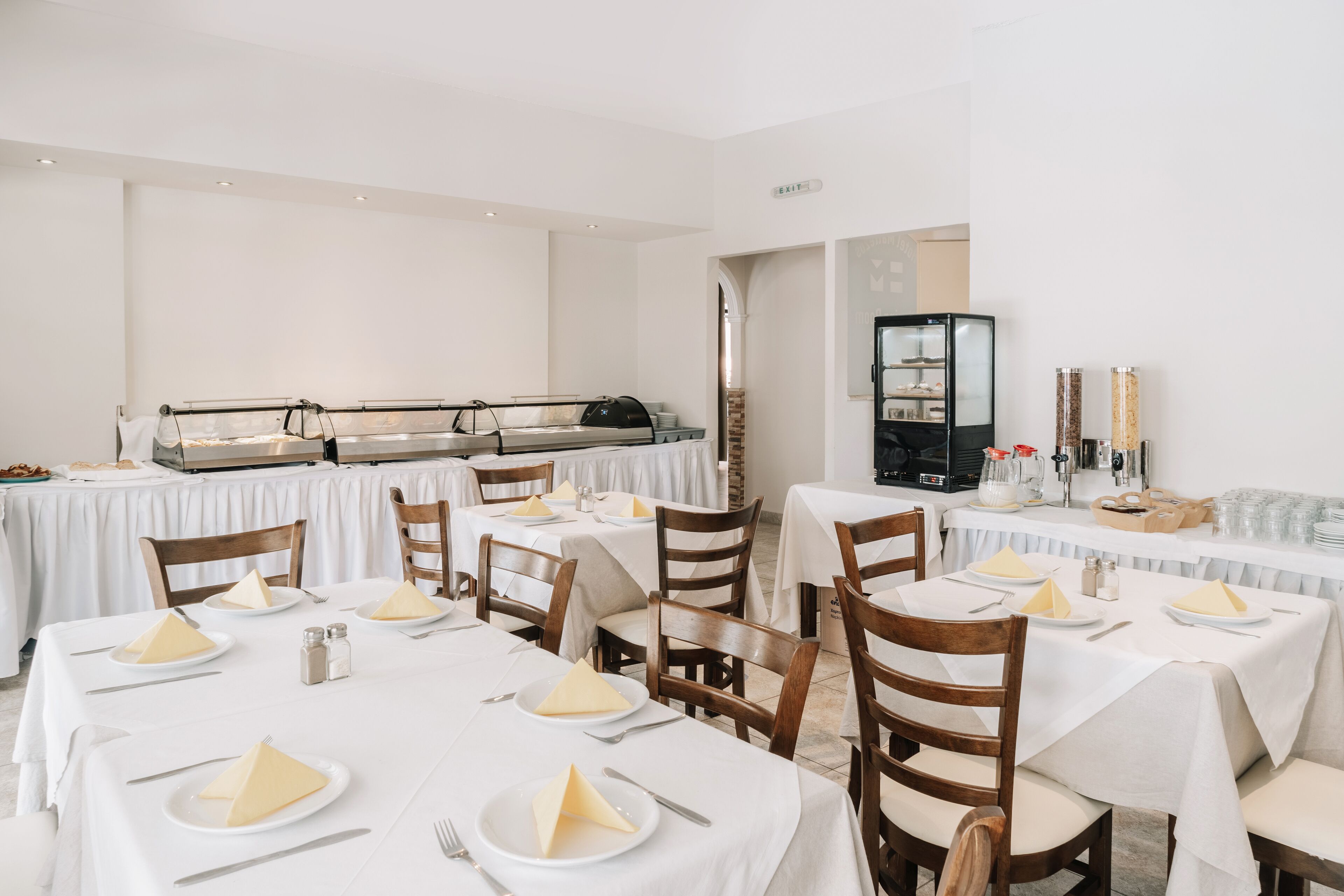 A restaurant with multiple tables set for dining, featuring white tablecloths and wooden chairs.