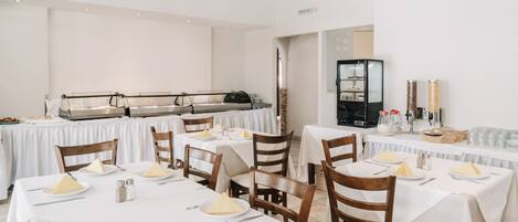 A restaurant with multiple tables set for dining, featuring white tablecloths and wooden chairs.