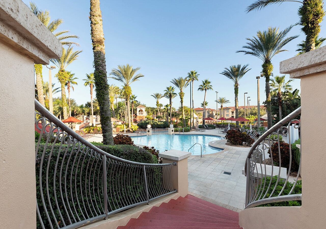 A pool area with palm trees, a red carpet, and a staircase leading to a balcony.