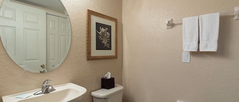 A bathroom with a sink, toilet, and a mirror. There is a framed picture on the wall and a towel rack with towels.