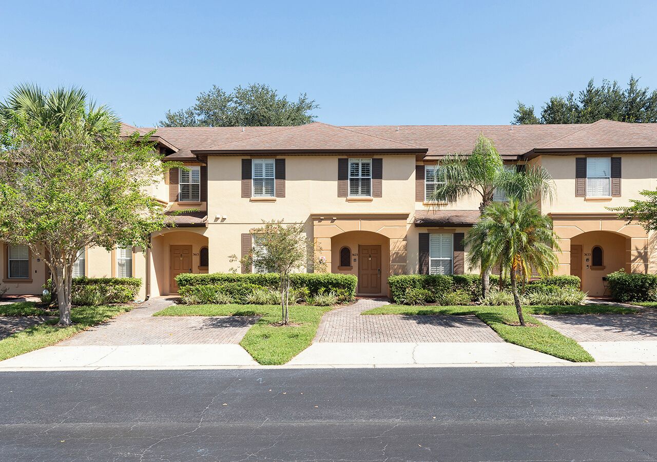 A row of townhouses with a uniform architectural style, featuring a central entrance, individual front doors, and a consistent roofline.