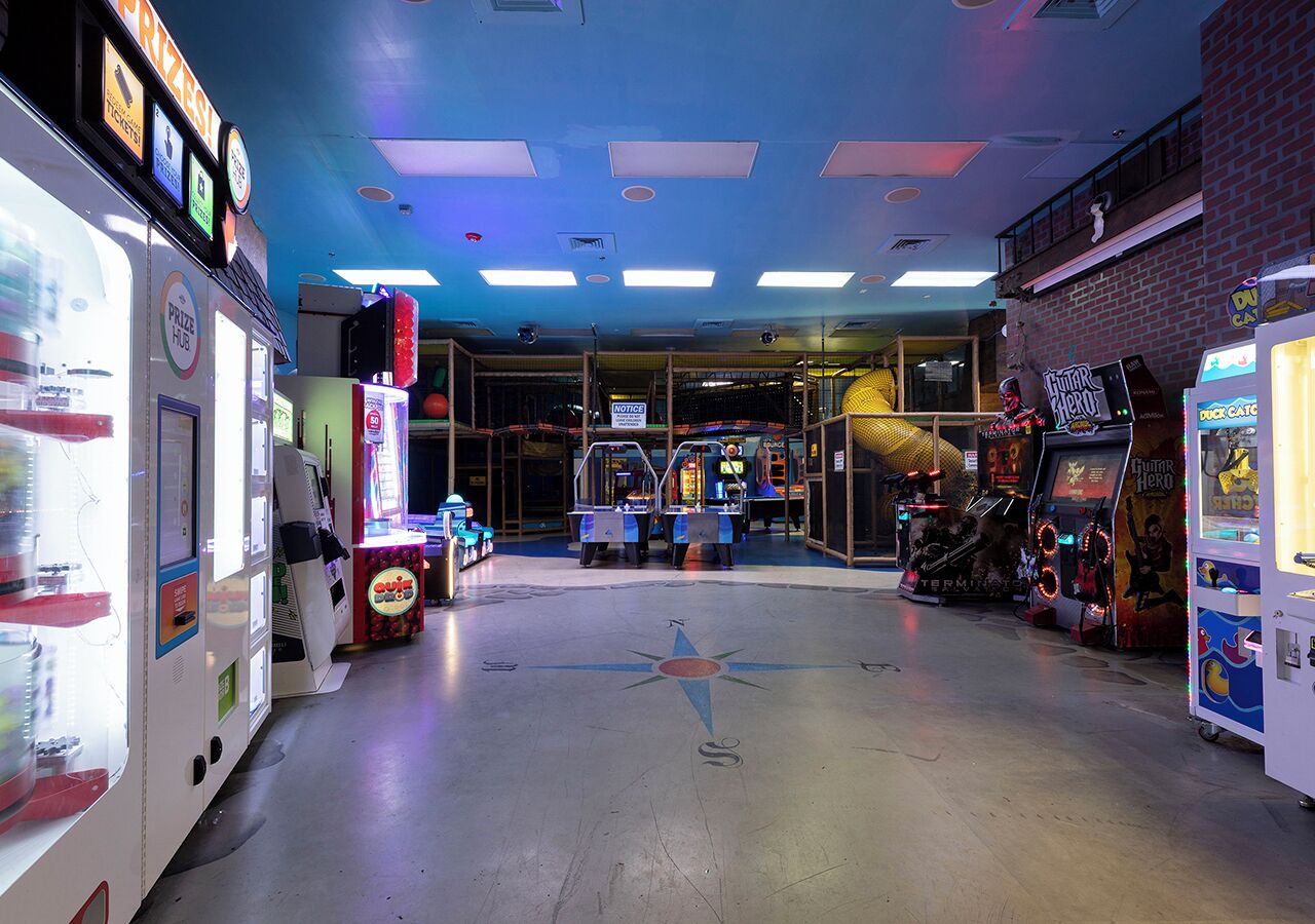 Un salón de juegos recreativos con diversas m áquinas y una zona central con un cartel.
