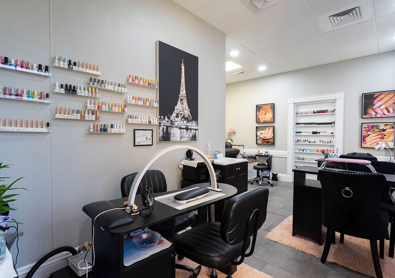 Un salón moderno con múltiples estaciones de tratamiento, un cartel grande de la Torre Eiffel y una variedad de botellas de esmalte de uñas en estantes.
