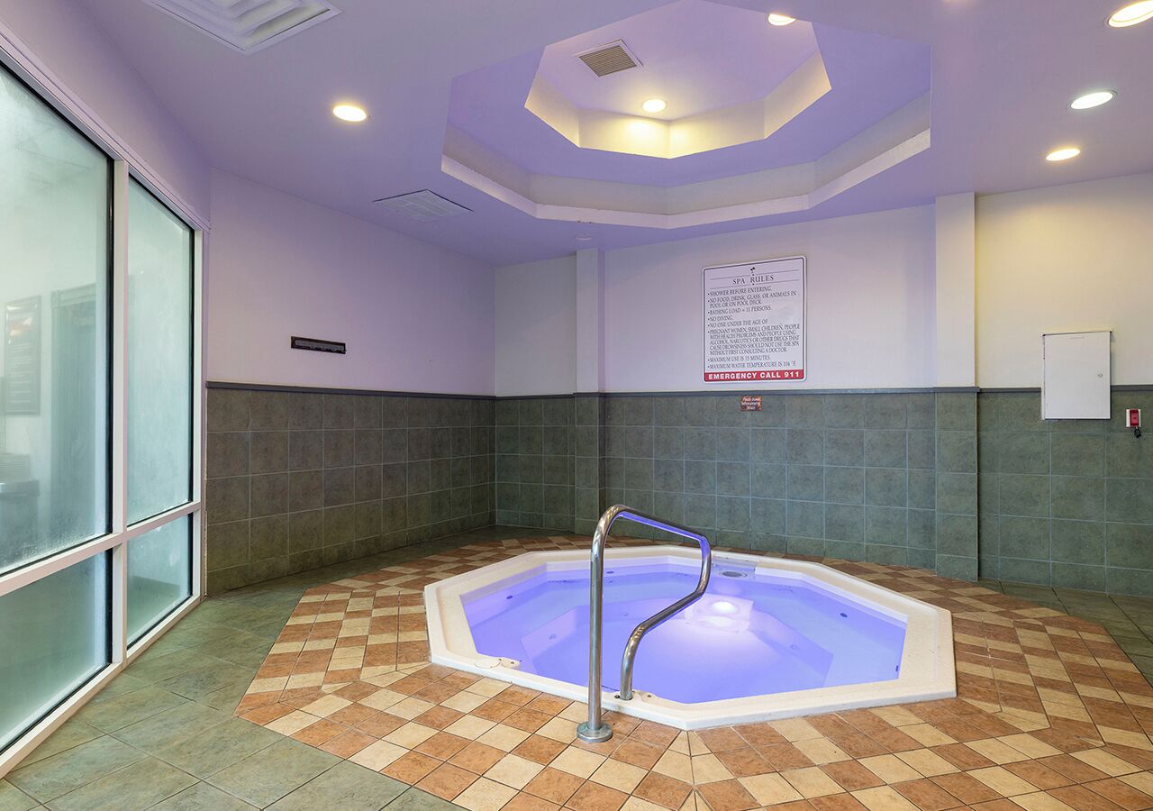 A spa area with a hot tub, a handrail, tiled walls, and a sign with emergency contact information.