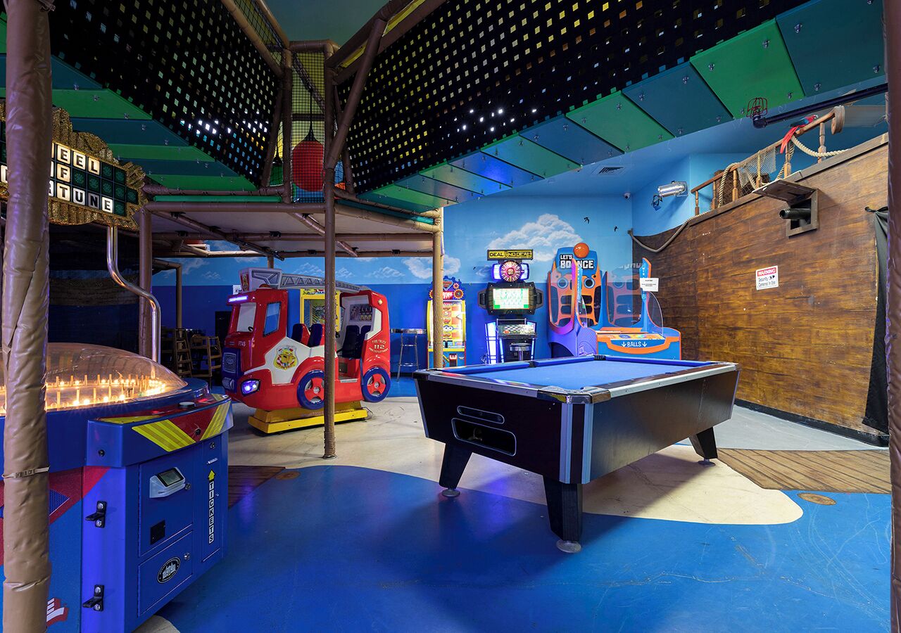 Een binnenspeelruimte met een pooltafel, speelautomaten en een kinderauto.