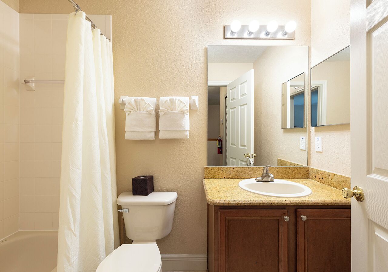 A bathroom with a shower, toilet, sink, and mirror.