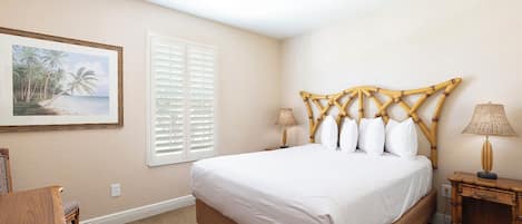 A bedroom with a large bed, a wooden nightstand, a lamp, a painting on the wall, and a window with blinds.