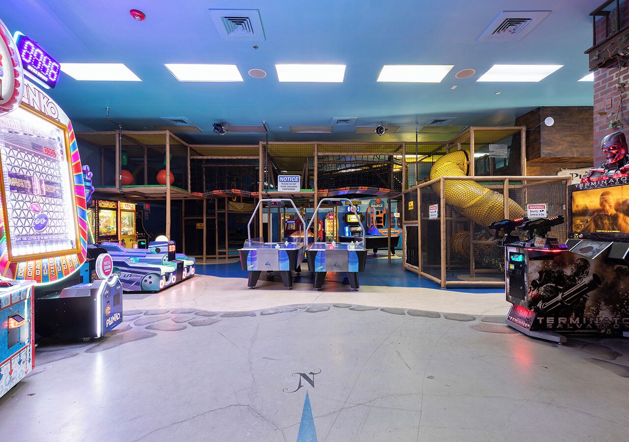 Une salle d’arcade intérieure proposant divers jeux, dont un jeu « DINO » très populaire et un autre jeu sur le thème de « TERMINATOR ».