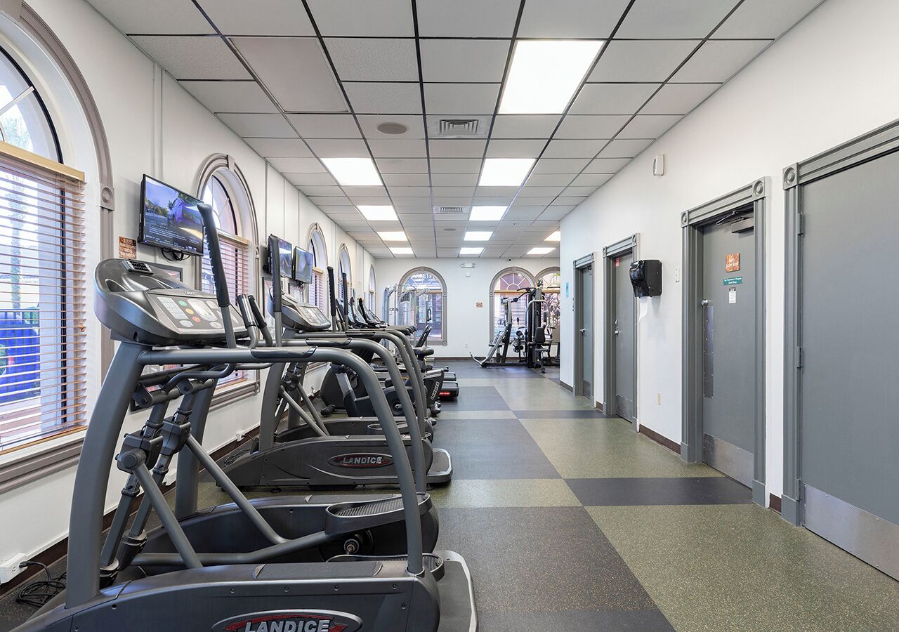 A gym with treadmills lined up along a corridor with windows and doors.