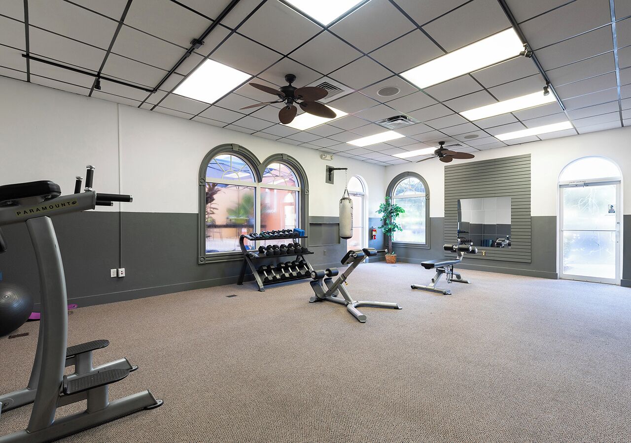 A gym with exercise equipment, large windows, and ceiling fans.