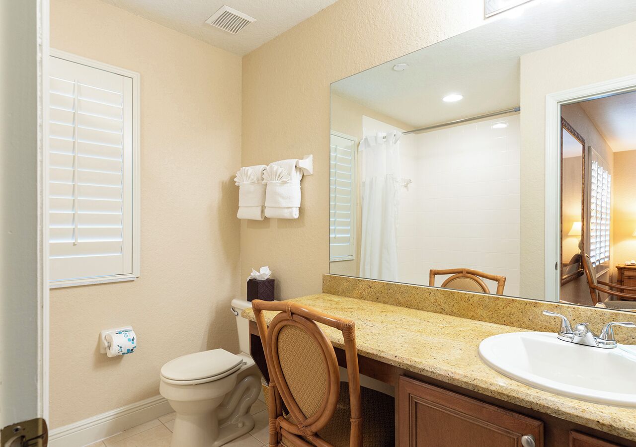 A bathroom with a toilet, sink, mirror, and a chair.