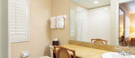 A bathroom with a toilet, sink, mirror, and a chair.
