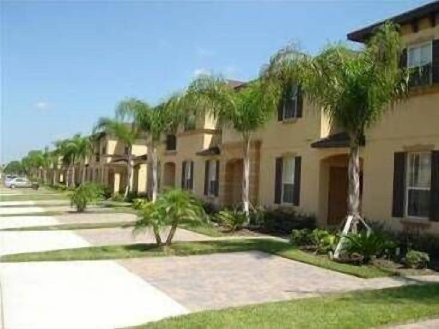 Una hilera de casas adosadas con un paseo central, cada una con un pequeño jardín delantero y palmeras.