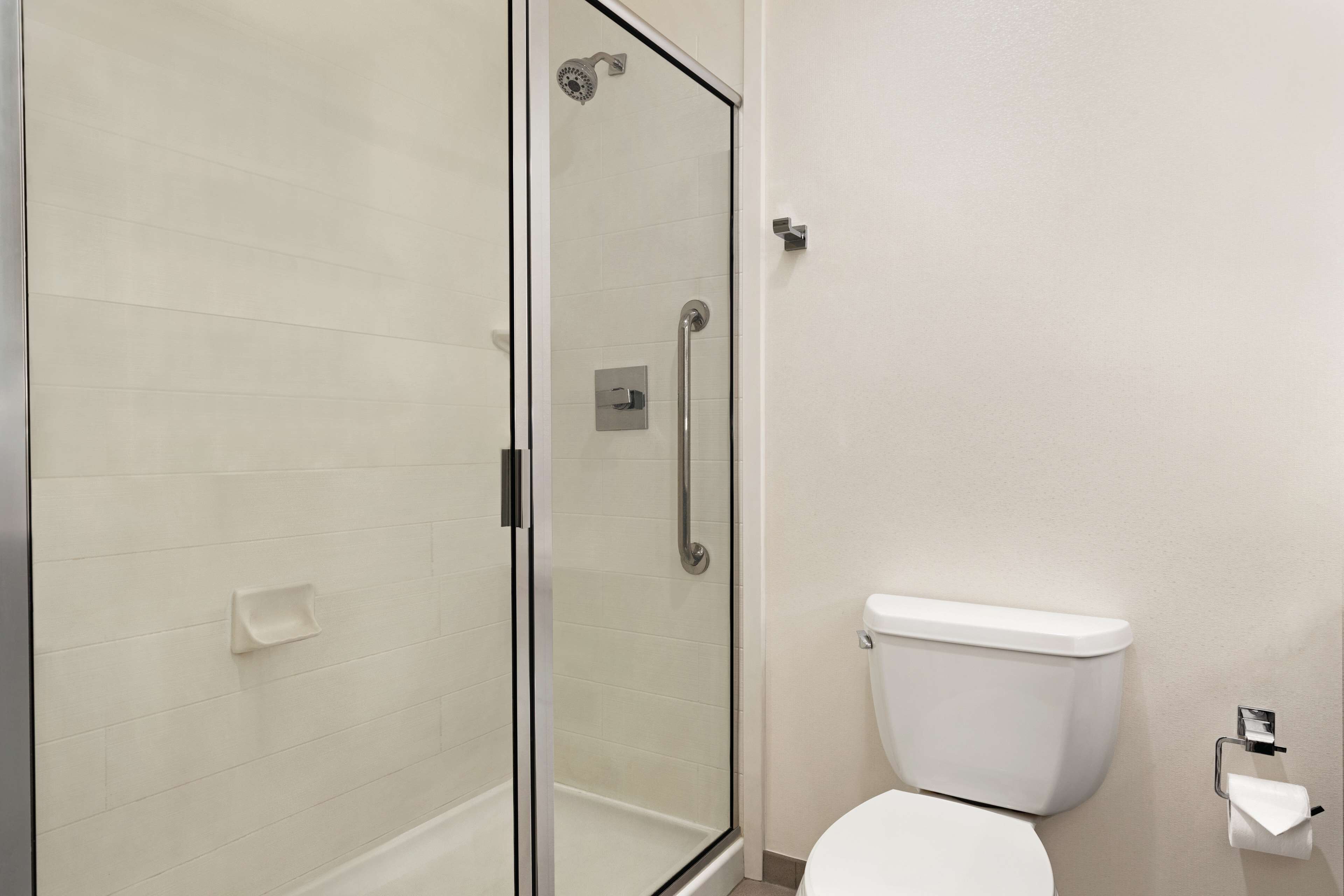 A bathroom with a glass shower enclosure, a white toilet, and a hand sanitizer dispenser.