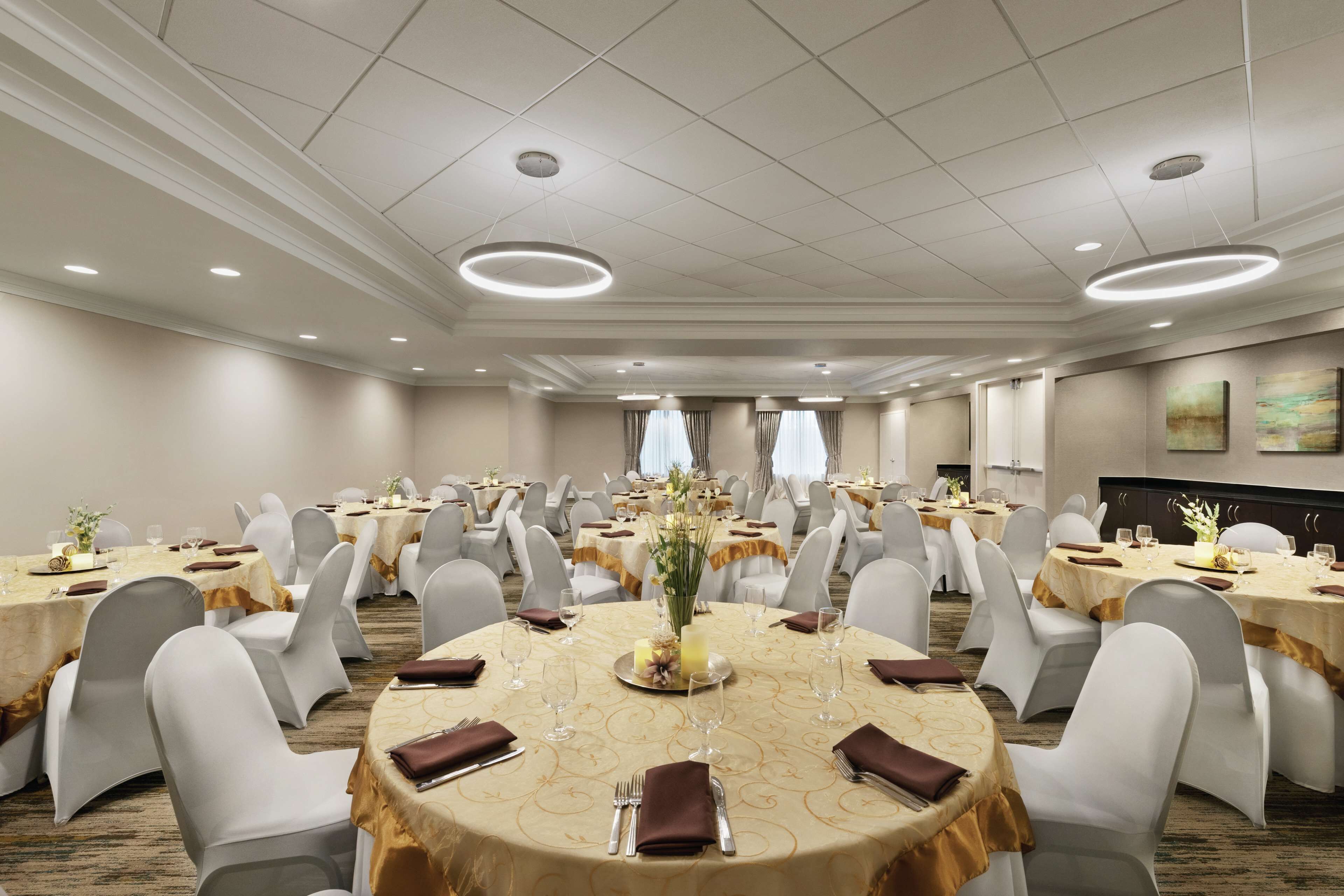 A banquet hall with round tables, white chairs, and gold tablecloths.