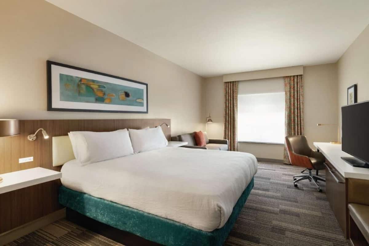 Habitación de hotel con cama, escritorio, silla, televisor y un cuadro en la pared.