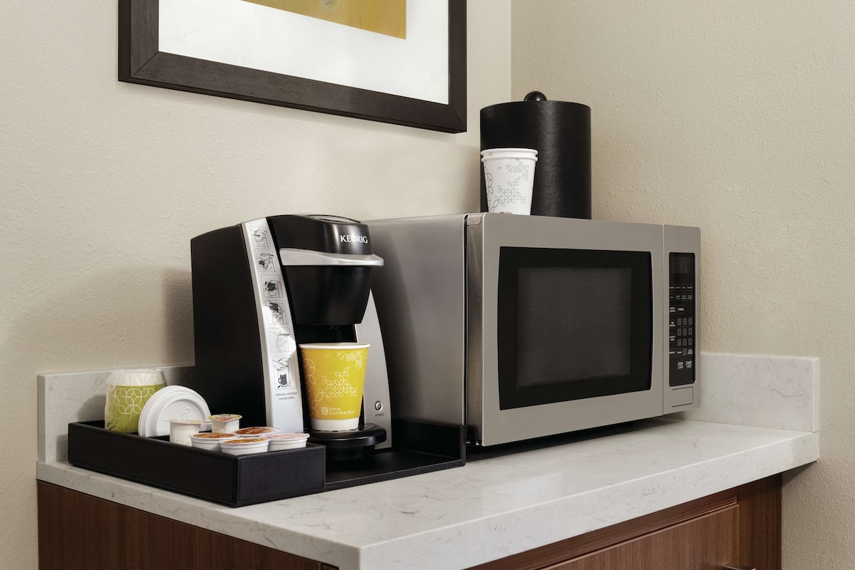 Una cocina con cafetera, microondas y una taza de café sobre la encimera.
